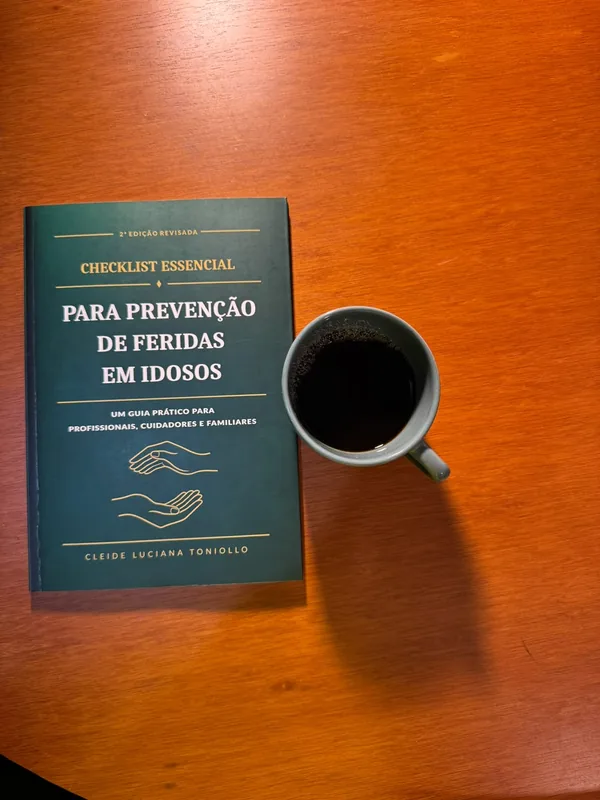 Livro Checklist Essencial para Prevenção de Feridas em Idosos ao lado de uma xícara de café